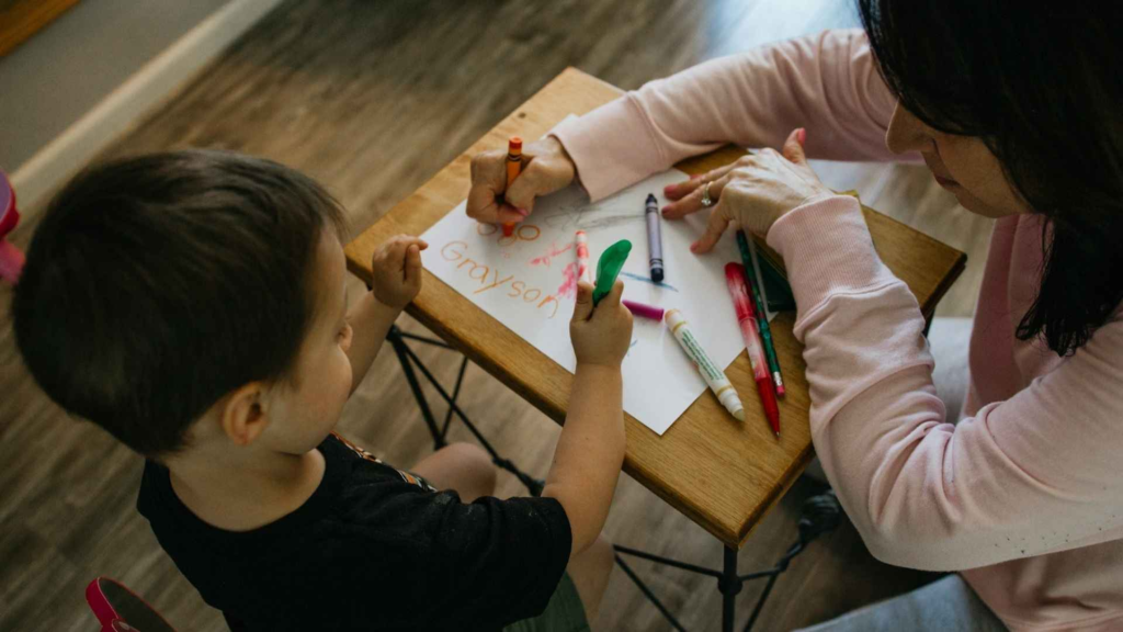 Preschool-aged child and adult drawing together with colorful markers during an at-home activity.