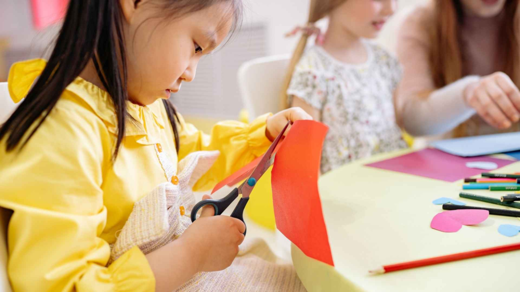 Preschool child cutting colorful paper during an indoor summer craft activity.