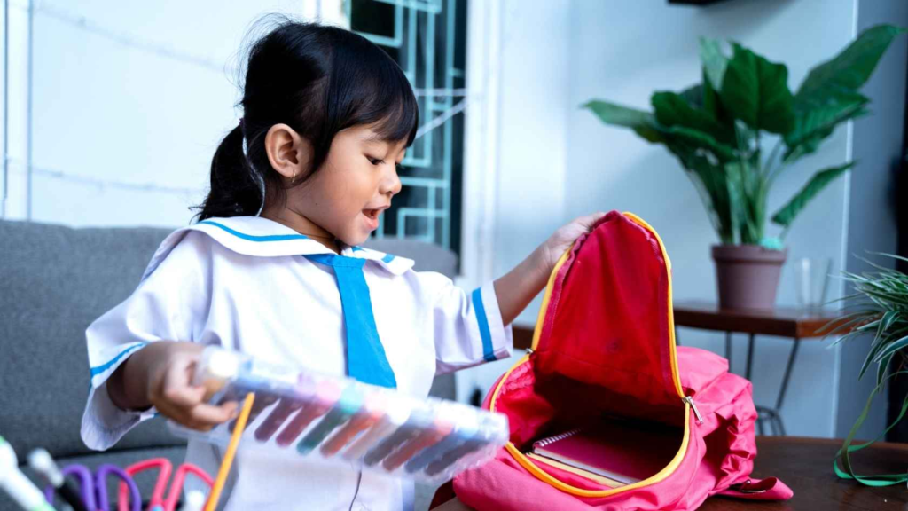 Young child packing school supplies into a backpack for preschool or kindergarten.