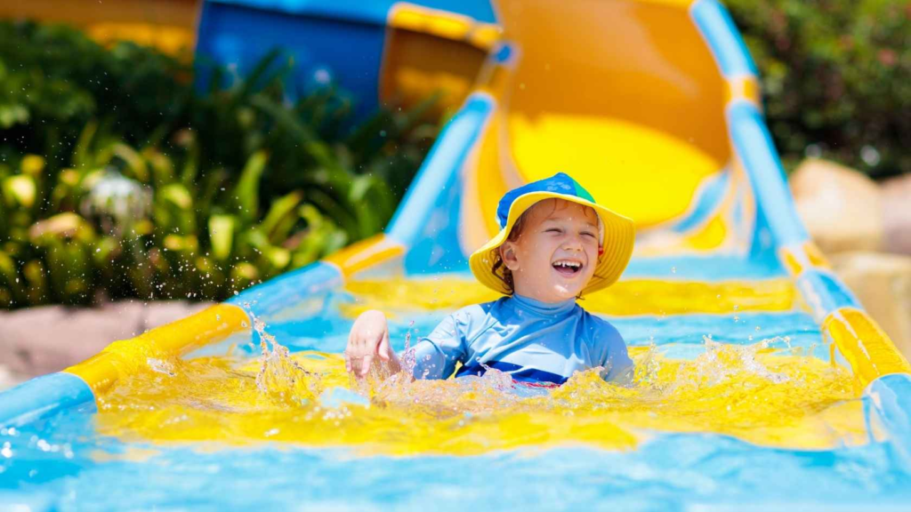 Young child smiling while playing on a colorful water slide during a summer activity.