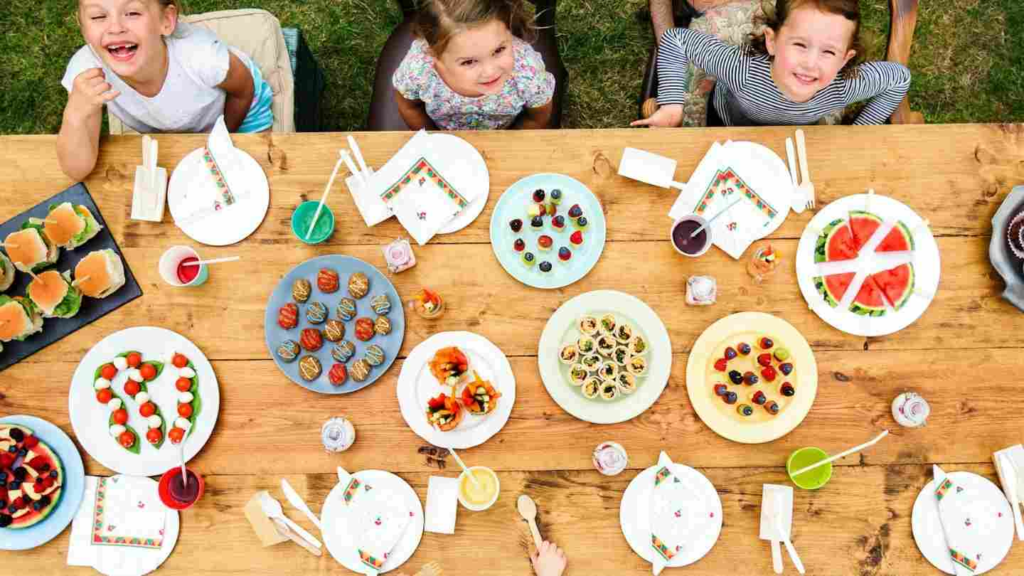 Children gathered around an outdoor table with healthy snacks and drinks.