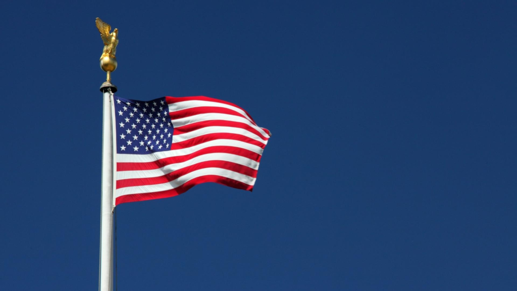 American flag waving against a clear blue sky for a Fourth of July celebration.