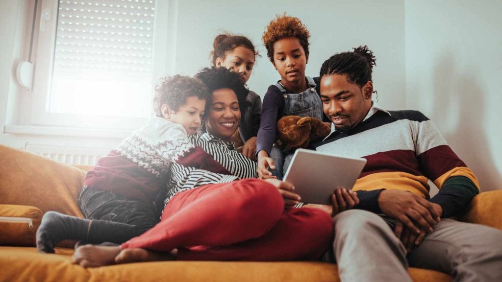 Family sitting together on a couch while children use a tablet for learning.