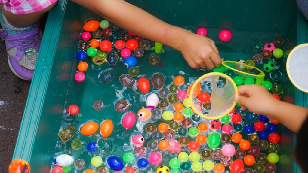 Children playing a colorful water game with floating toys and small nets.