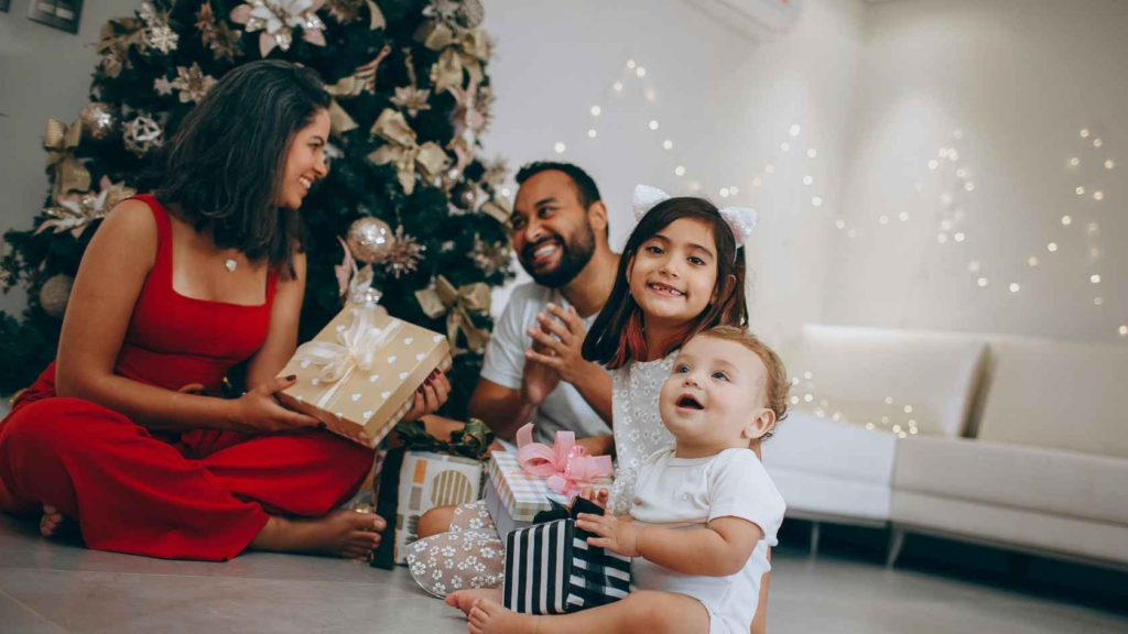 Family celebrating Christmas together while opening gifts beside a decorated Christmas tree.