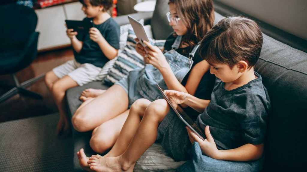 Young children sitting on a couch while using tablets for screen-based learning.