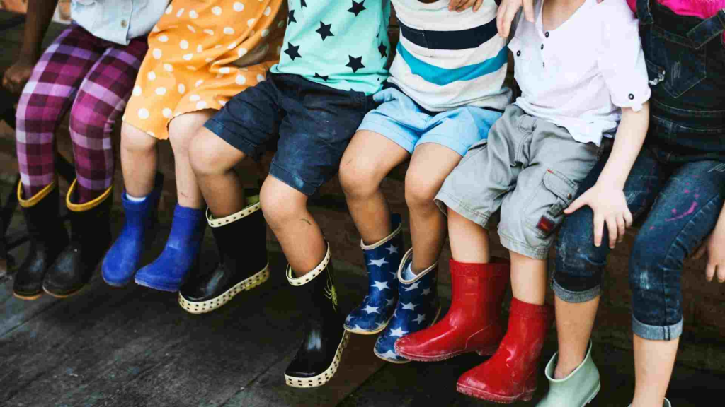Group of young children sitting together while wearing colorful rain boots.
