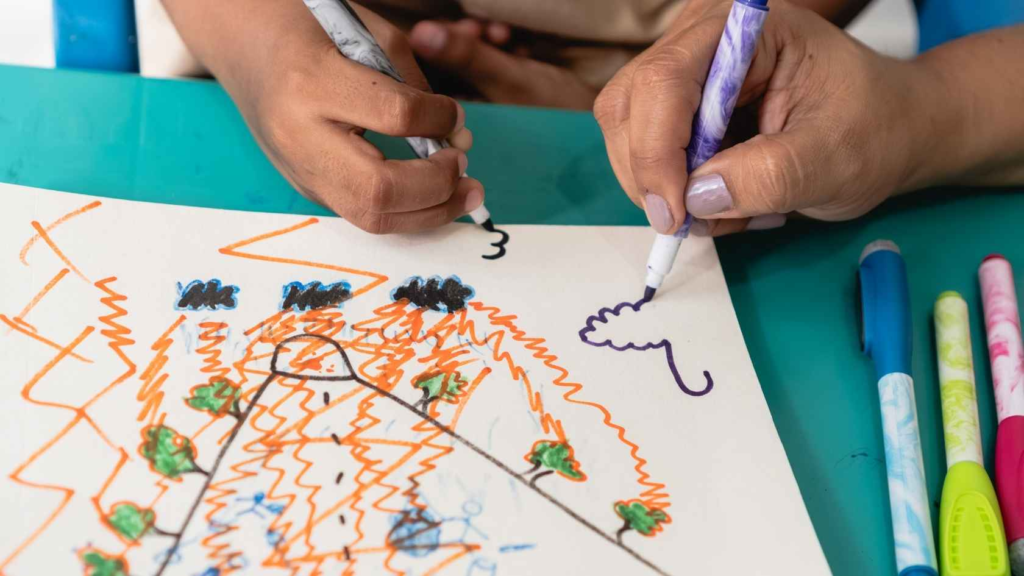 Child and adult drawing together with markers during an early learning activity.