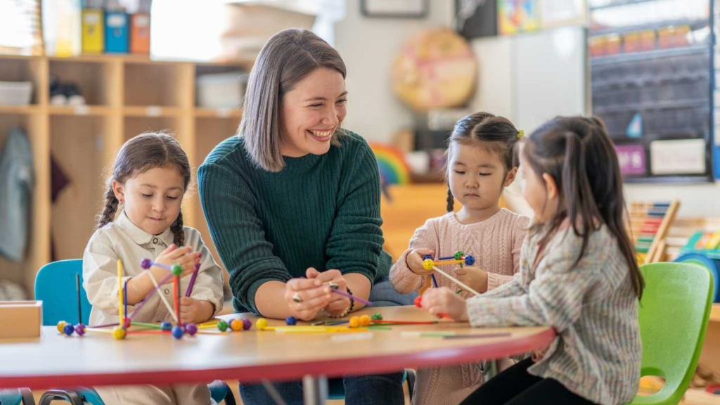 Daycare teacher sitting with young children during a hands-on classroom activity.