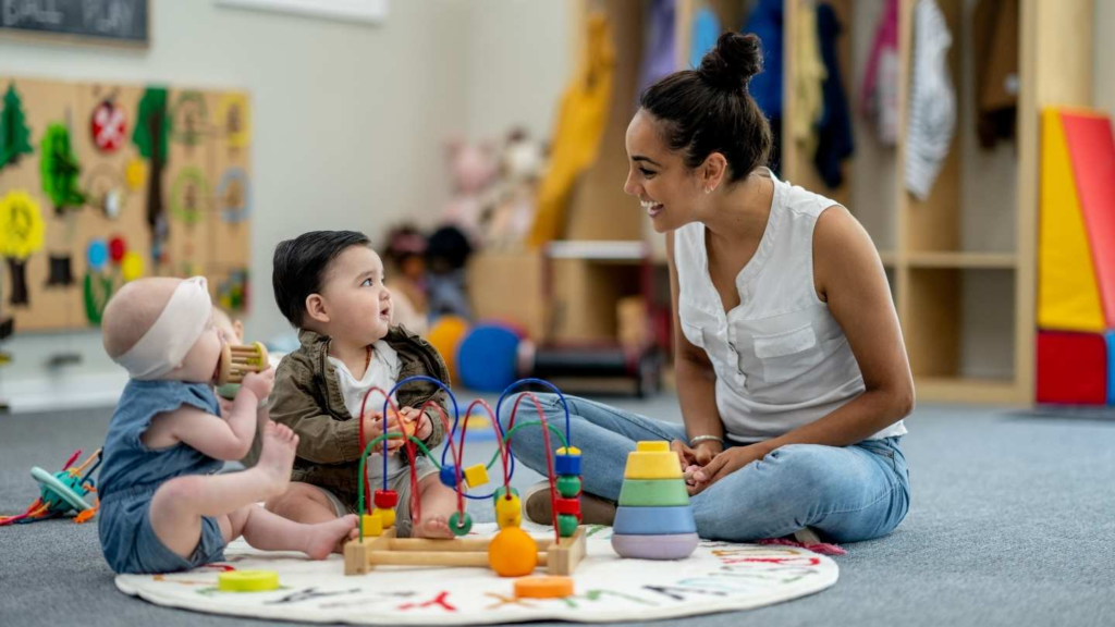 Daycare teacher sitting with infants and toddlers during supervised playtime.