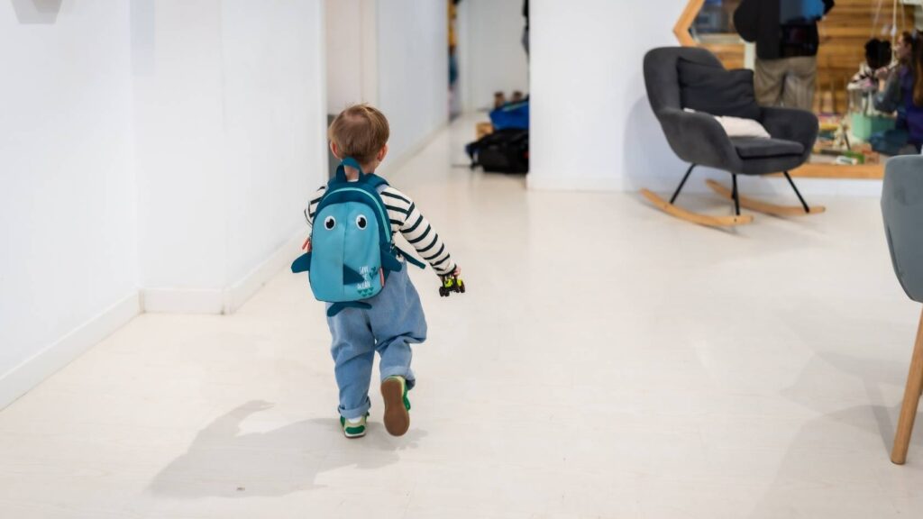 Young child wearing a backpack walking into a daycare or early learning center.